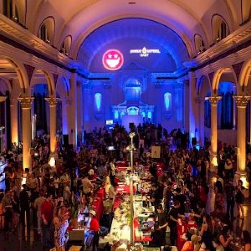 Elegant venue with arched ceilings, people gathered at an event with colorful lighting and decorations.