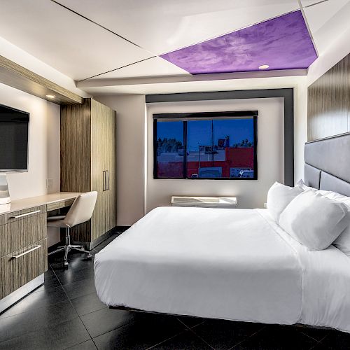 Modern hotel room with a bed, nightstands, TV, desk, and city view window.