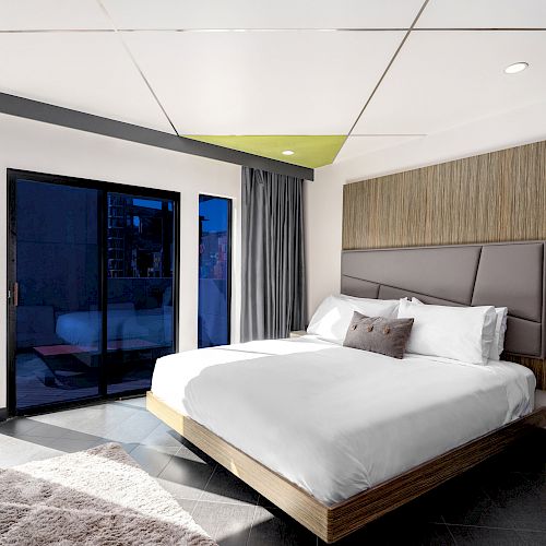 Modern bedroom interior with king bed, balcony doors, and chic decor.