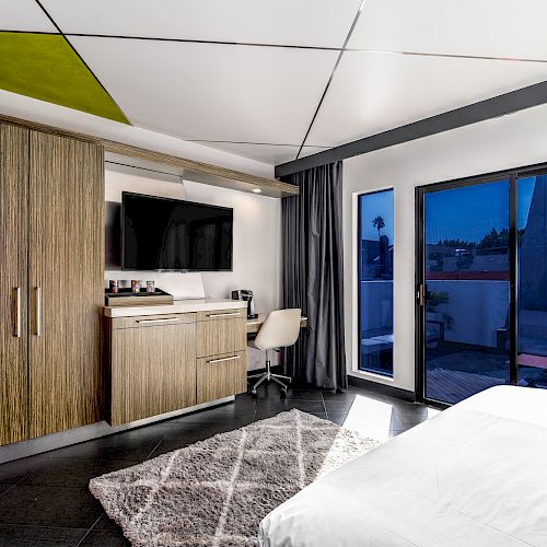Modern hotel room with a bed, desk, and sliding door leading to a balcony.