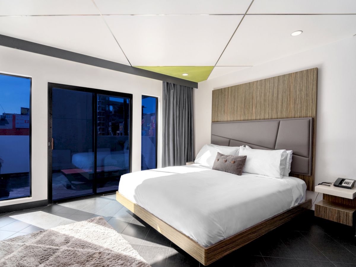 Modern hotel room with bed, desk, and balcony access.